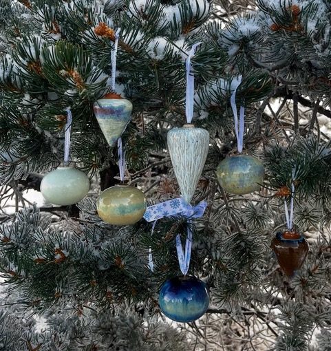 Glazed ceramic ornaments hanging in a snowy pine tree