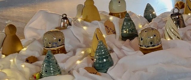 Glazed ceramic trees, bells and luminaries on a white cloth with string lights