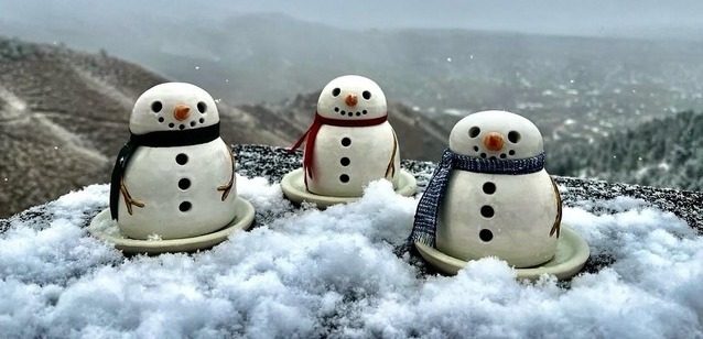 Three small ceramic snowmen with scarves sitting in fresh snow