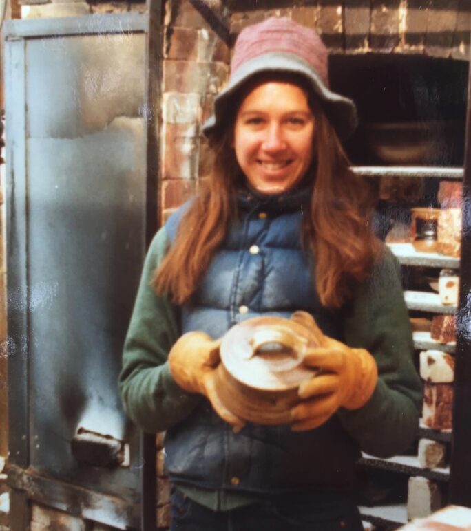 A young Ellen Nadeau holding a pot at a wood and salt kiln